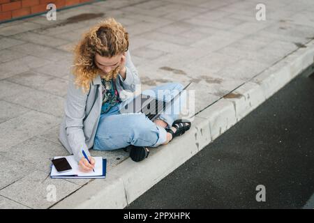 Student learning online using laptop studying outside campus, elearning using laptop computer onthe street, watching online webinar. Education Stock Photo