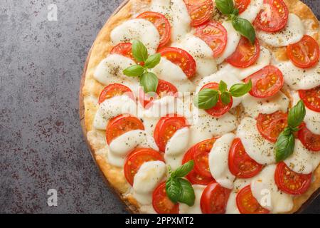Caprese pizza topped with mozzarella, tomatoes, basil a little salt and pepper, and a drizzle of olive oil close-up on a wooden board on the table. Ho Stock Photo