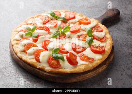 Freshly baked Caprese pizza with cheese, tomatoes and basil close-up on a wooden board on the table. horizontal Stock Photo