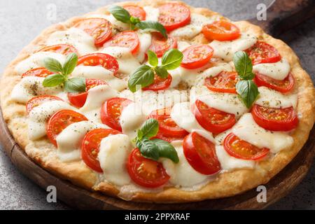 Caprese pizza with melted mozzarella, tomatoes and basil leaves close-up on a wooden board on the table. horizontal Stock Photo