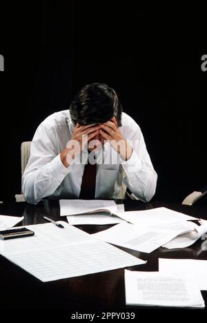 Business executive with a headache in a pile of paperwork shot on a black background Stock Photo