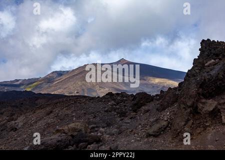 peak of mount etna on sicily dormant on a clear day with a wall of solid lava in the foreground Stock Photo