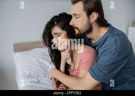 Bearded man hugging dissatisfied girlfriend with napkin in bedroom,stock image Stock Photo