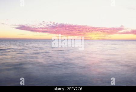 Sun setting behind clouds and over calm tropical ocean Stock Photo