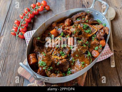 Braised beef shanks or ossubuco with gravy and root vegetables in a old fashioned roasting pan isolated on wooden table from above Stock Photo