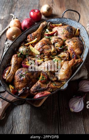 Braised chicken with onions and apples in a old fashioned roasting pan isolated on wooden table Stock Photo