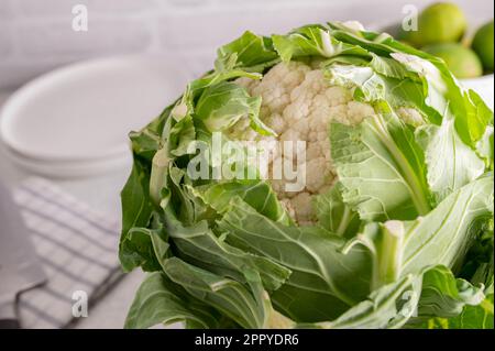 Cauliflower with green leaves on white kitchen counter Stock Photo