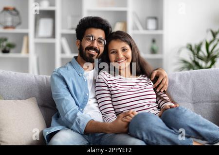 Portrait of cheerful eastern couple cuddling on couch at home Stock Photo