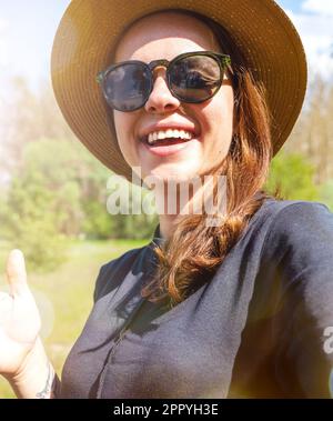 Happy woman wearing sunglasses and straw hat takes a selfie outdoors and smiling. Stock Photo
