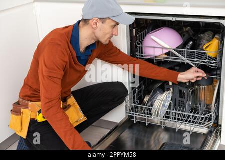 A man or a service worker in special clothes using a screwdriver attaches to the countertop or removes the dishwasher. Stock Photo