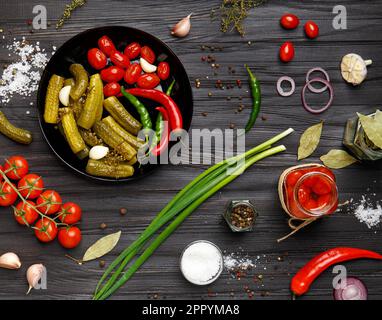 Assorted pickled vegetables. Canned tomatoes, cucumbers, chili peppers in a round black plate on a dark background. appetizer of canned vegetables. Stock Photo