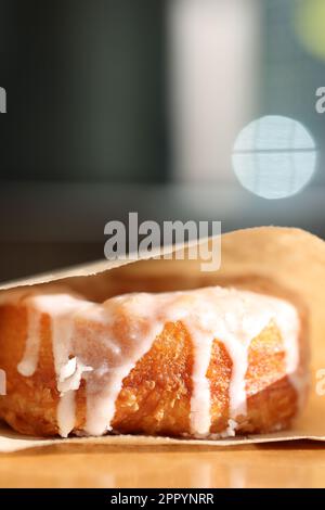 A freshly-baked donut enclosed in a paper bag, placed on a table surface Stock Photo