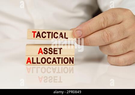 Business concept. In the hands of a person and on a reflective surface are wooden blocks with the inscription - Tactical Asset Allocation Stock Photo