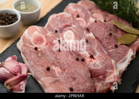 View from above of a table with raw lamb meat chops, with spices such as bay leaf, peppercorns, garlic, rosemary Stock Photo