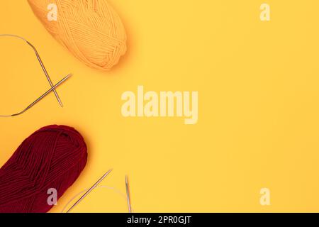 Knitting needles and skeins of wool threads on a yellow background. Leisure concept with copy space. Stock Photo
