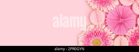 Banner with gerbera flowers, tissue paper fans and balls on a pink background. Stock Photo
