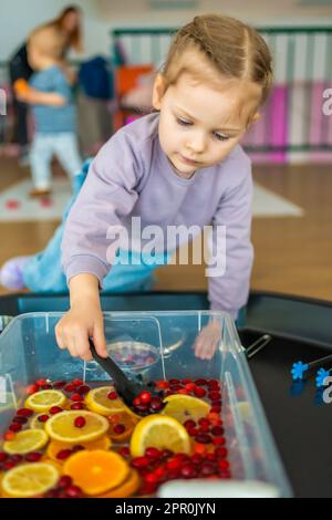 Little girl playing in handmade fruit bar with kitchenware, berries and citrus fruits. Sensory development and experiences, themed activities with Stock Photo