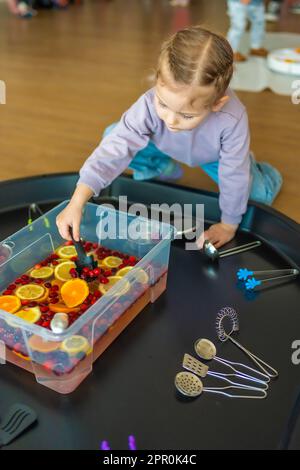 Little girl playing in handmade fruit bar with kitchenware, berries and citrus fruits. Sensory development and experiences, themed activities with Stock Photo