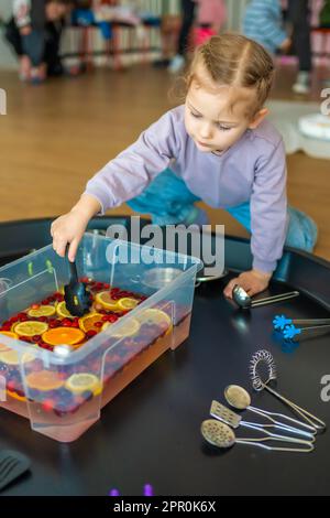 Little girl playing in handmade fruit bar with kitchenware, berries and citrus fruits. Sensory development and experiences, themed activities with Stock Photo