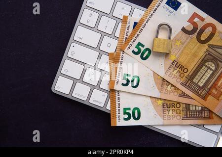 Closed padlock on some euro bills on a laptop frame. Keep our savings safe. Space for copy text. Dark background. Stock Photo