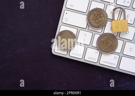 Closed padlock on some euro coins on a laptop frame. Keep our savings safe. Space for copy text. Dark background. Stock Photo