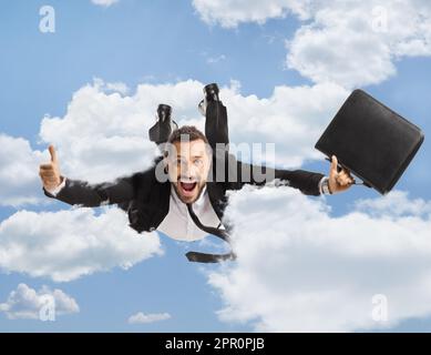 Businessman with a briefcase flying and gesturing thumbs up up in the sky Stock Photo