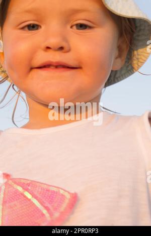 Portrait of a smiling blonde little toddler girl in a pink t-shirt and blue panama close up Stock Photo