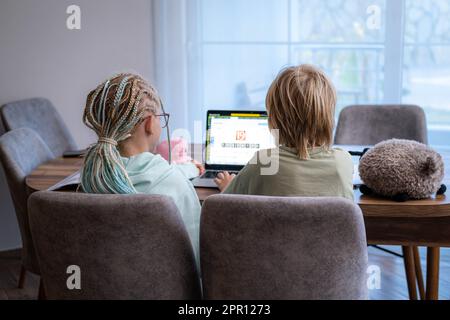 back view siblings pupils boy and girl learning together remotely online at home, looking to laptop, speaking with teacher or tutor using internet Stock Photo