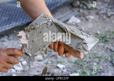 Man putting wet paste cement mortar mix on masonry trowel with metal spattle, one hand blurred to emphasise action, closeup detail Stock Photo