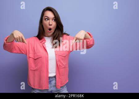 shocked black haired lady in casual style pointing finger at wall in studio background Stock Photo
