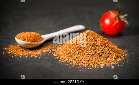 Spices on a spoon and a bunch of dried sun-dried tomatoes next to cherry tomato on the table. Stock Photo