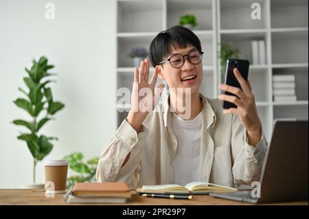 Young happy Asian man having a video call with his family, sitting at his study table. Stock Photo