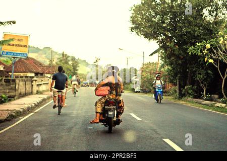 Motorists and cyclists on a road in Klungkung, Bali, Indonesia. Stock Photo