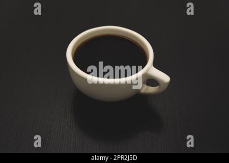 Black coffee in a classic American diner-style white cup sits on a black table. Stock Photo