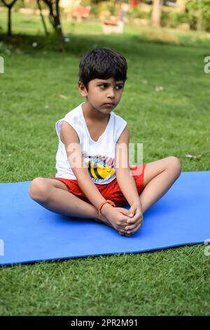 Asian smart kid doing yoga pose in the society park outdoor, Children's yoga pose. The little boy doing Yoga and meditation exercise. Stock Photo