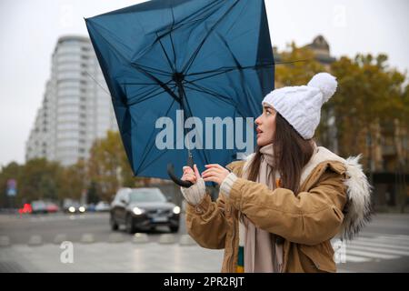 Woman with blue umbrella caught in gust of wind on street Stock Photo