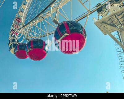 Ferris wheel in the city center against the blue sky. red booths rise in a row, rolling tourists. sightseeing tour on the carousel. ride on the attrac Stock Photo