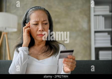 Stressed and unhappy Asian mature woman having financial problems or problems with her credit card payment. Stock Photo