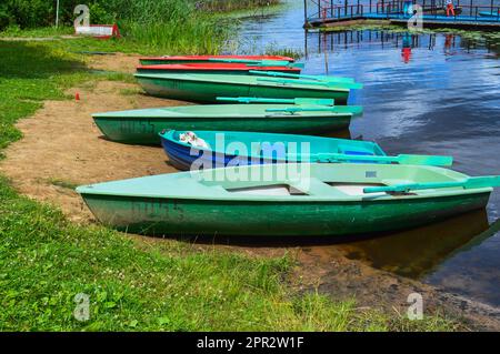 Beautiful wooden multicolored boats with oars on the beach for walks along the river, lake, sea, ocean in a nature park on the shore. Stock Photo