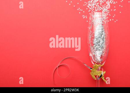 Shiny confetti spilled out of champagne glass on red background, top view. Space for text Stock Photo