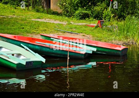 Beautiful wooden multicolored boats with oars on the beach for walks along the river, lake, sea, ocean in a nature park on the shore. Stock Photo