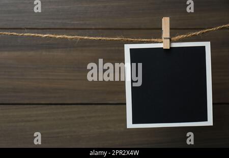 Clothespin with empty instant frame on twine against wooden background. Space for text Stock Photo