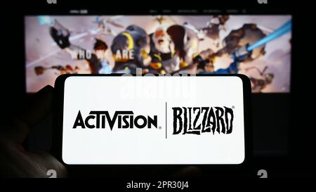 Person holding cellphone with logo of American video game company Activision Blizzard Inc. on screen in front of webpage. Focus on phone display. Stock Photo