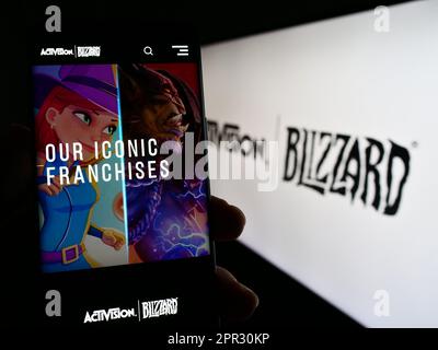 Person holding mobile phone with webpage of US video game company Activision Blizzard Inc. on screen with logo. Focus on center of phone display. Stock Photo