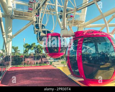 Ferris wheel in the city center against the blue sky. red cabins with sliding doors on a wheel for tourists to ride. booths are made of durable metal Stock Photo