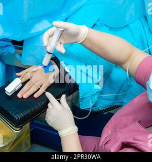 The doctor injects an anesthetic drug with a syringe through a catheter into the patient's wrist. Anesthetizing a patient during surgery. Stock Photo