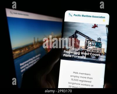 Person holding cellphone with webpage and logo of organization Pacific Maritime Association (PMA) on screen. Focus on center of phone display. Stock Photo