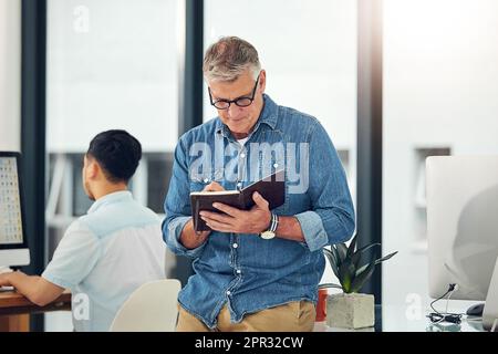 Penning down some fresh ideas. a creative entrepreneur making notes in his notebook while standing in the office. Stock Photo