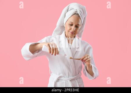 Mature woman with toothbrush and paste on pink background Stock Photo