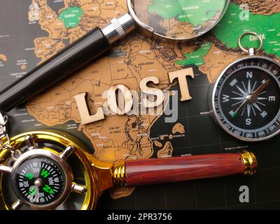 Magnifying glass,compass with the wooden word LOST on a world map background. Stock Photo